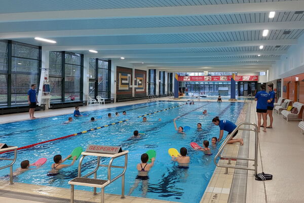 Illustrierte Szene eines Schwimmkurses für Kinder im Hallenbad - geduldige Ausbilder, kleine Gruppen